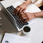 Person typing on a computer at a desk with cup of coffee next to them.