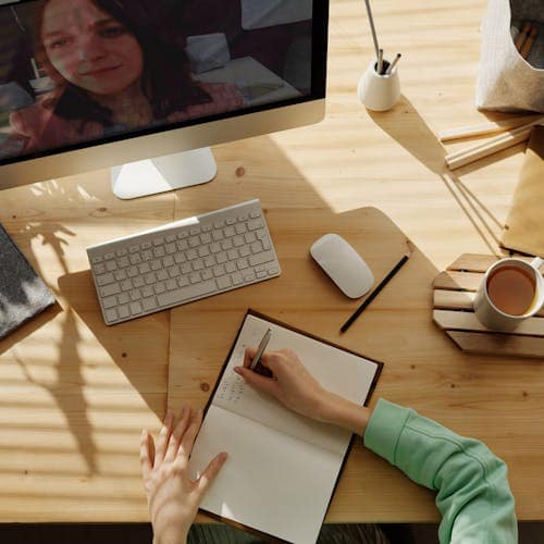 How the Ghostwriting Process Works: Woman writing in notebook while conducting a Zoom interview.