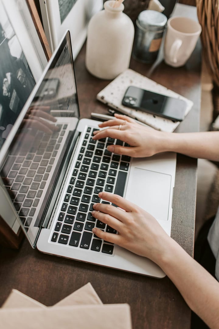 Woman typing on a laptop at a desk with a phone beside the laptop